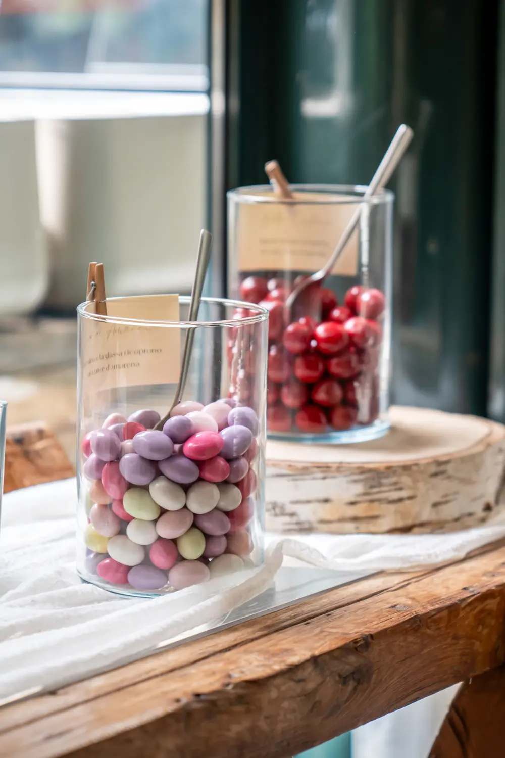 Due barattoli di confetti, uno di lilla e rosa e uno di rossi, con le palette