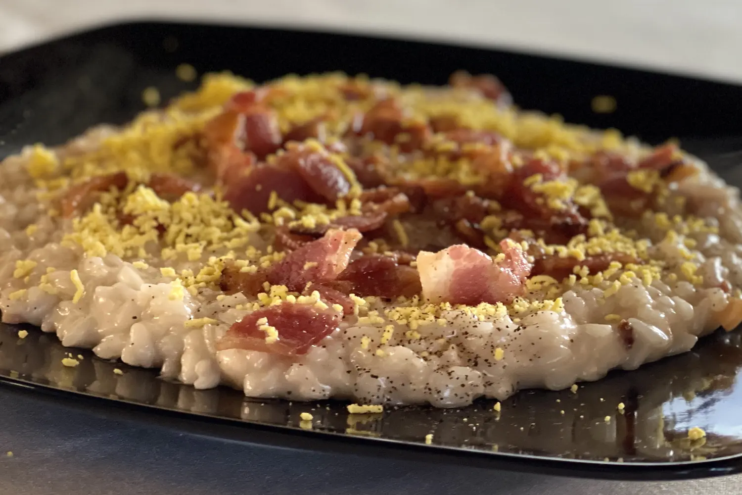 Risotto con speck croccante e granella di formaggio su piatto quadrato nero