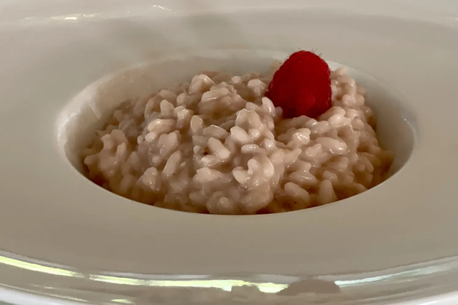 Risotto mantecato con un lampone al centro, piatto fondo bianco