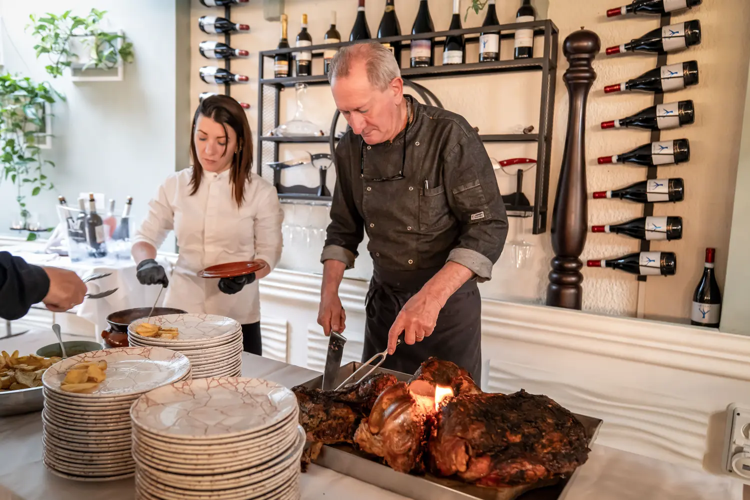 Chef e cameriera impiattano l'arrosto, parete di bottiglie