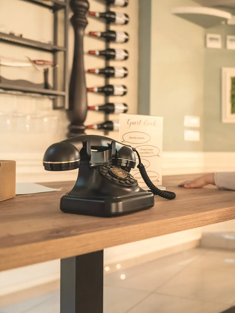 Un telefono vintage nero su un tavolo di legno, accanto a un cartoncino "Guest Book" e a una parete di bottiglie di vino.
